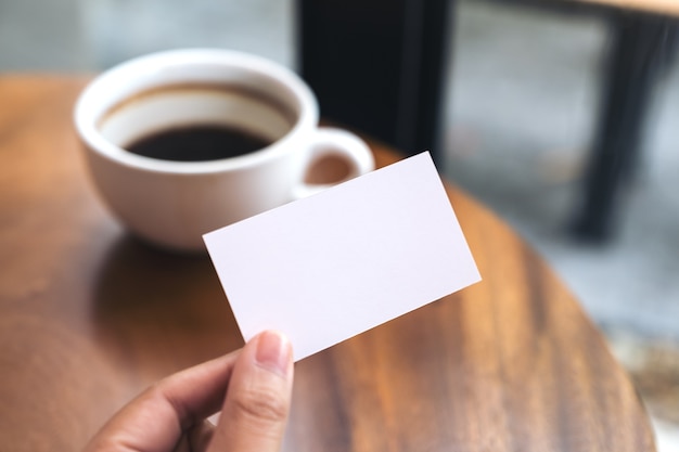 Mani che tengono un biglietto da visita e una tazza di caffè vuoti