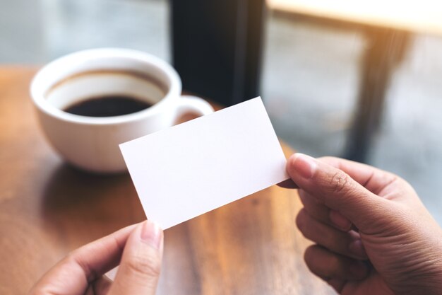 Hands holding an empty business card with coffee cup on table