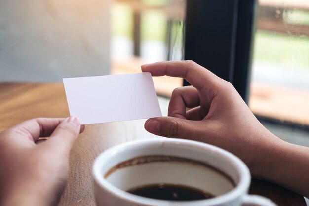 Hands holding an empty business card with coffee cup on table