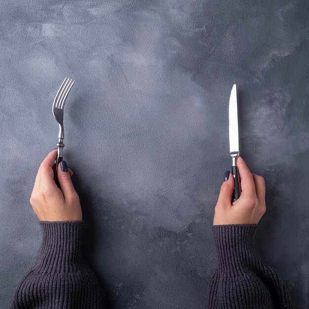 Photo hands holding fork and knife on gray surface. top view