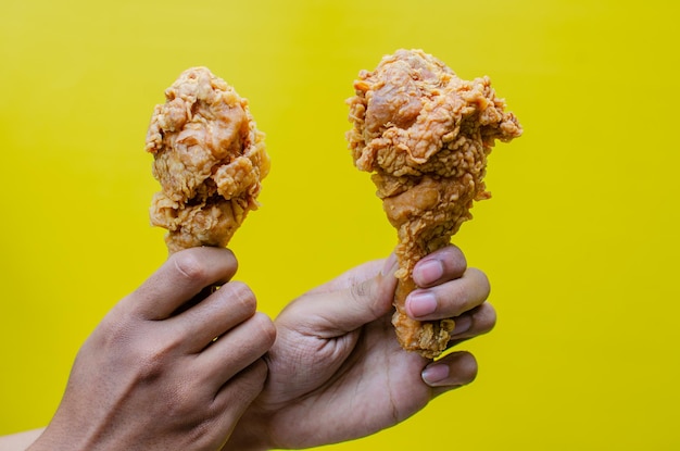 Фото Руки, держащие жареную курицу, изолированные на желтом фоне, вкусная хрустящая жареная курица