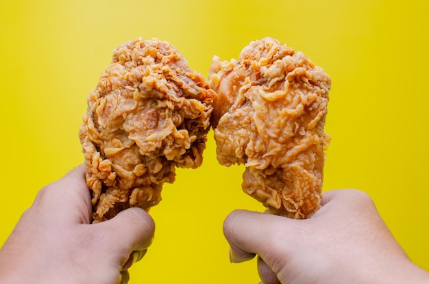 Hands holding fried chicken isolated on yellow background tasty crispy fried chicken drumstick