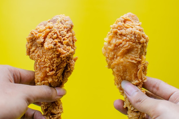 Hands holding fried chicken isolated on yellow background tasty crispy fried chicken drumstick