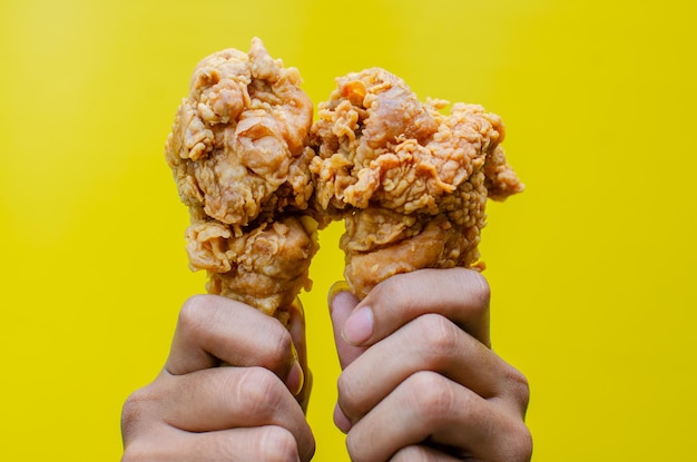 Руки, держащие жареную курицу, изолированные на желтом фоне, вкусная хрустящая жареная курица