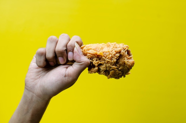 Hands holding fried chicken isolated on yellow background tasty crispy fried chicken drumstick