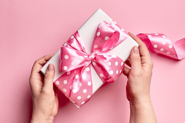 Mani che tengono confezione regalo con grande fiocco su sfondo rosa