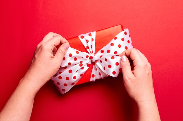 Hands holding gift box with big bow on red