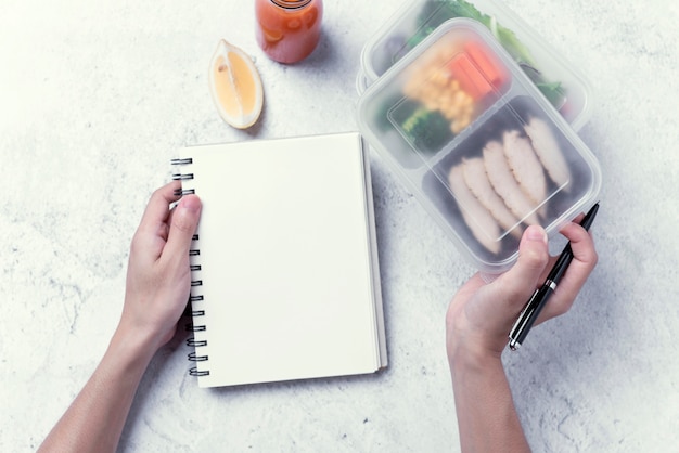 Hands holding healthy lunch box and blank notebook for your text message or design, order food .