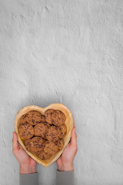 Hands holding heart shape plate with traditional chocolate chip cookies