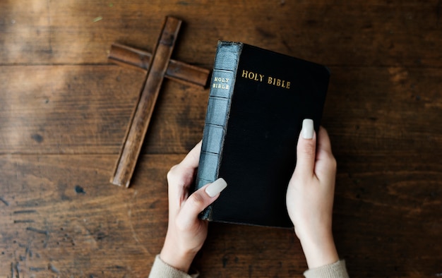 Mani che tengono la bibbia santa accanto alla croce di legno