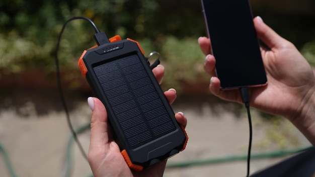 Hands holding mobile phone with external battery connected to it with solar battery closeup