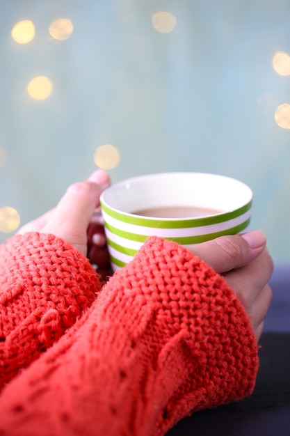 Hands holding mug of hot drink, close-up, on bright background