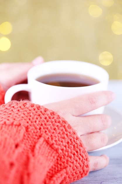 Hands holding mug of hot drink, close-up, on bright background