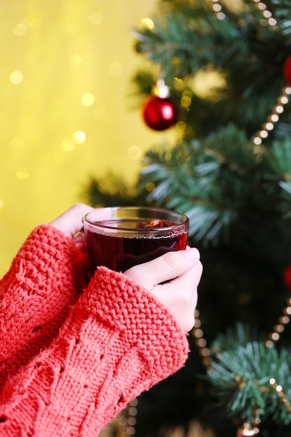 Hands holding mug of hot drink, close-up, on Christmas tree background