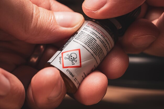 Hands holding nicotine eliquid bottle with danger warning symbol closeup view