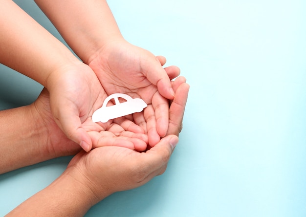 hands holding paper car shape on blue.