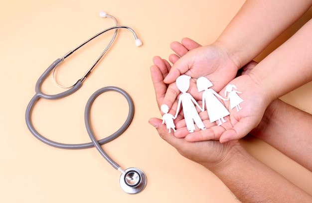 hands holding paper family cutout with stethoscope.