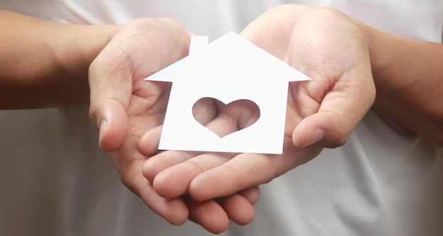 Hands holding paper house, family home and protecting insurance concept