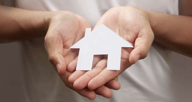 Hands holding paper house, family home and protecting insurance concept