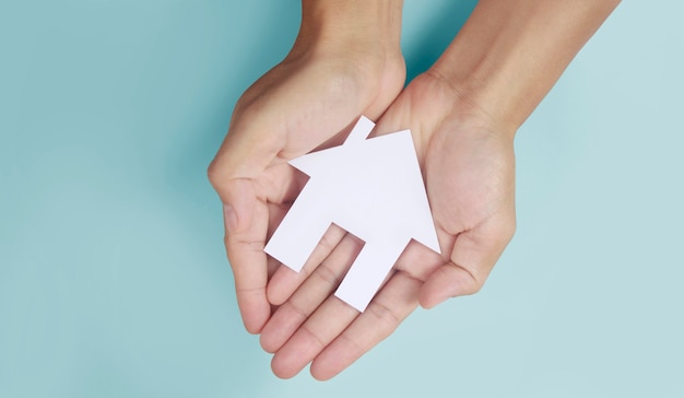 Hands holding paper house, family home and protecting insurance concept