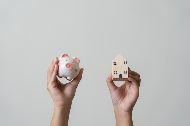 Hands holding piggy bank and small wooden house concept of savings property investment