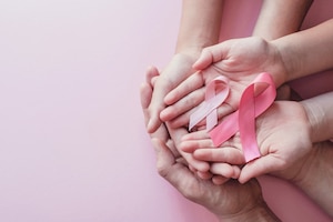 Hands holding pink ribbons on pink background