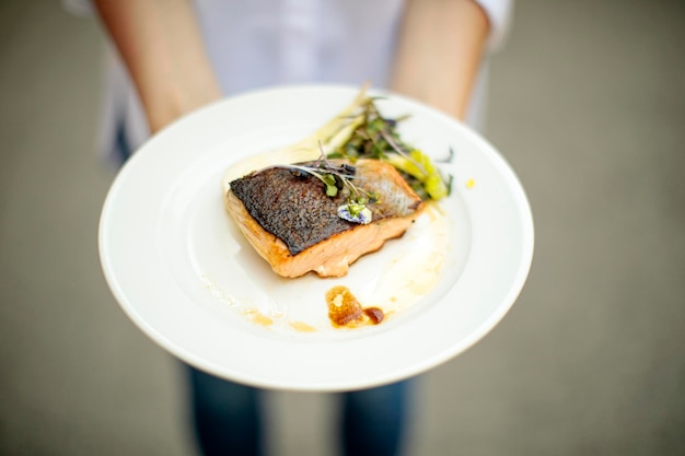 Photo hands holding a plate of cooked fish