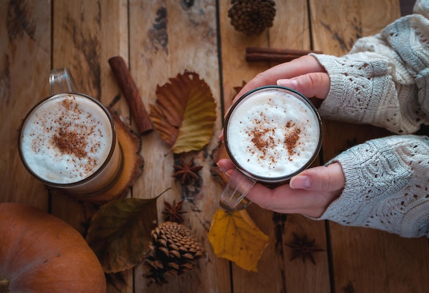 Photo hands holding pumpkin spice latte in glass cup on wooden background