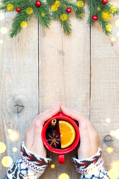 Hands holding red ceramic cup with mulled wine on wooden table,\
top view