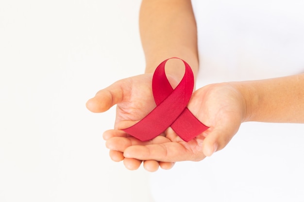 HIVエイズとともに生きる人々の連帯の象徴である赤いリボンを持った手。