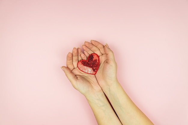 Hands holding red sequin heart on pink surface