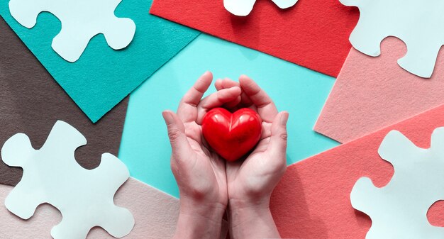 Mani che tengono il cuore di pietra rosso design creativo per la giornata mondiale dell'autismo di aprile