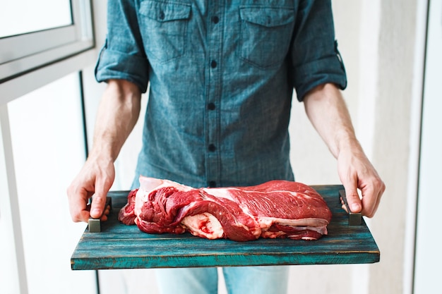 Hands holding rustic tray with raw beef meet