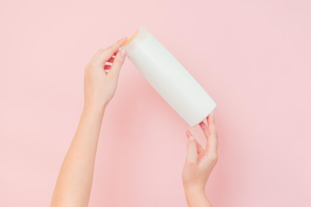 Hands holding shampoo hair conditioner or body lotion bottle in pink background Cosmetics bottle