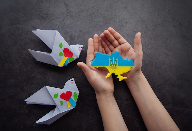 Hands holding the shape of ukraine border with color flag and\
paper birds stand with ukraine