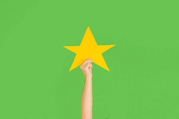 Hands holding the sign of star on green studio background