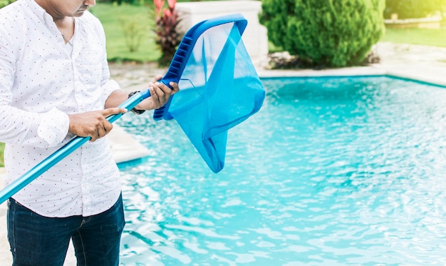 背景に青いプールのあるスキマーを持っている手葉のスキマーでプールを掃除している男スキマーでプールを掃除している男スキマーの掃除プールで人