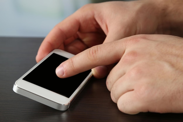 Руки держат смарт-мобильный телефон на деревянном столе и светлом размытом фоне