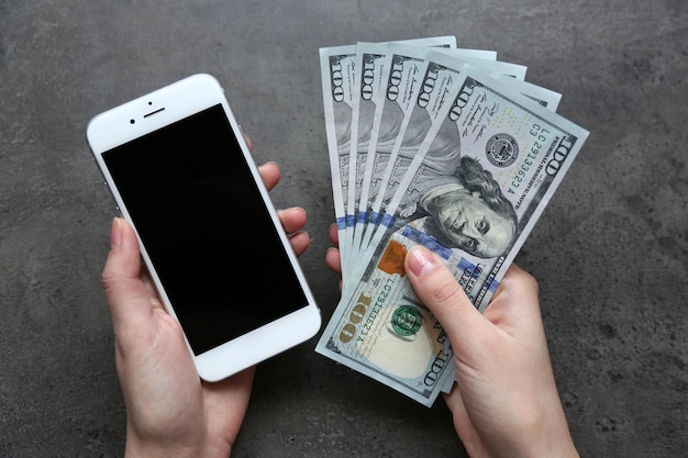 Hands holding smart phone with dollar banknotes on grey background Making money online