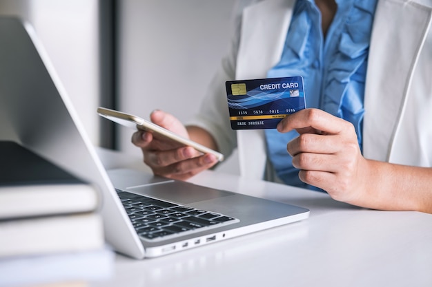 Hands holding smartphone, credit card and typing on laptop for online shopping and payment purchase