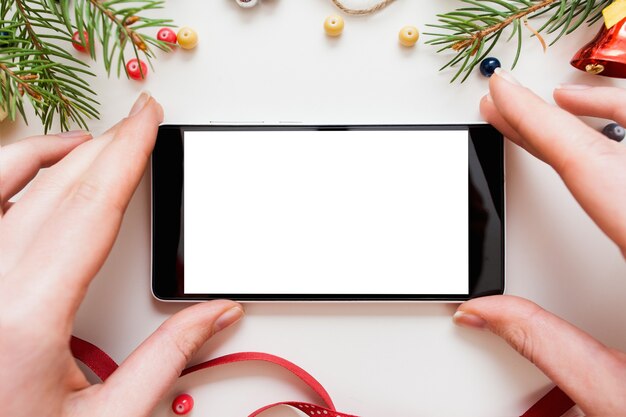 クリスマストランペリーのフレームで空白の画面でスマートフォンを保持している手、