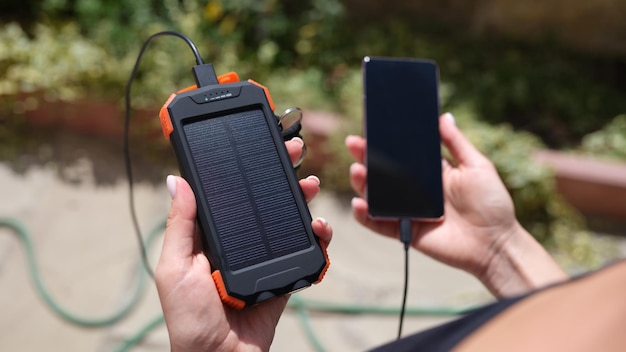 Photo hands holding a solar energy bank and mobile phone for recharging