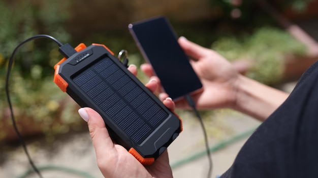 Mani che tengono la banca di energia solare e il telefono cellulare per ricaricare il primo piano