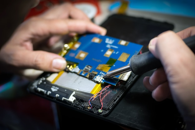 Hands holding a soldering iron close-up. Mobile phone repair and tablet