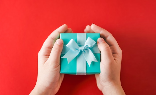 Hands holding a turquoise gift box on a red surface