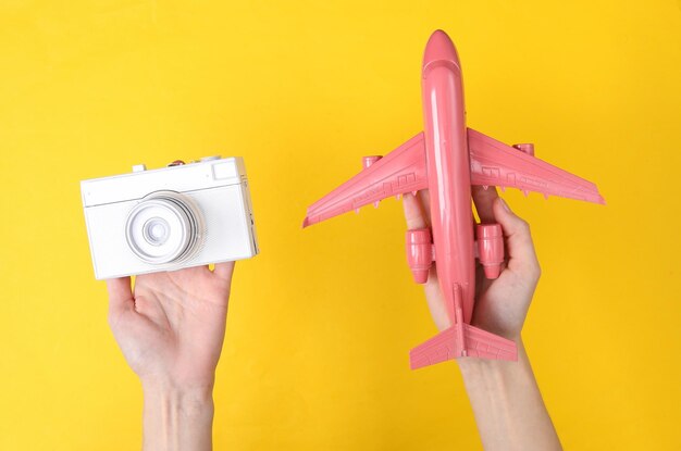 Hands holding white camera and pink air plane on yellow background Minimalism travel concept