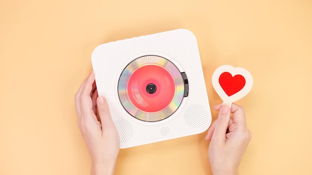 Hands holding white cd player with red disc and heart shape gift card on yellow Love Valentine day