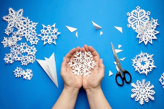 Hands holding white cutted paper snowflake on blue surface