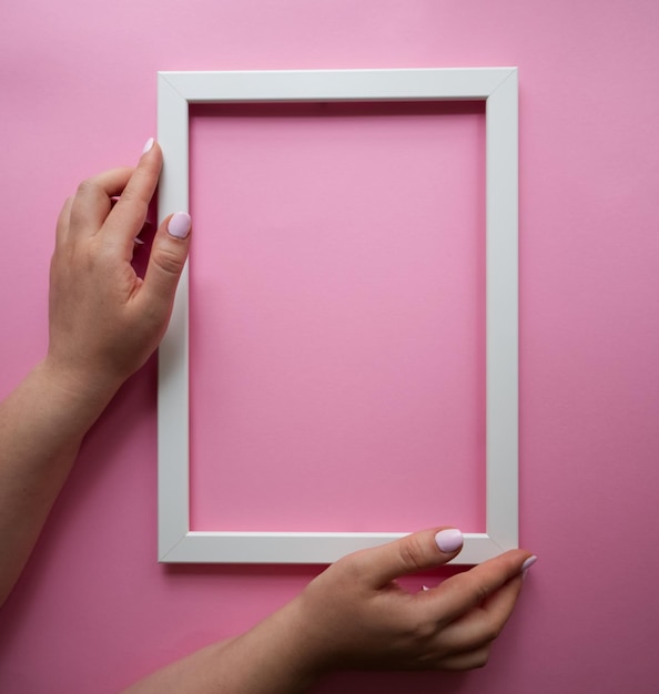 Hands holding a white frame on a pink background