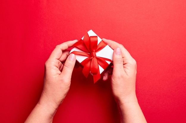 Hands holding white gift box with red ribbon on red